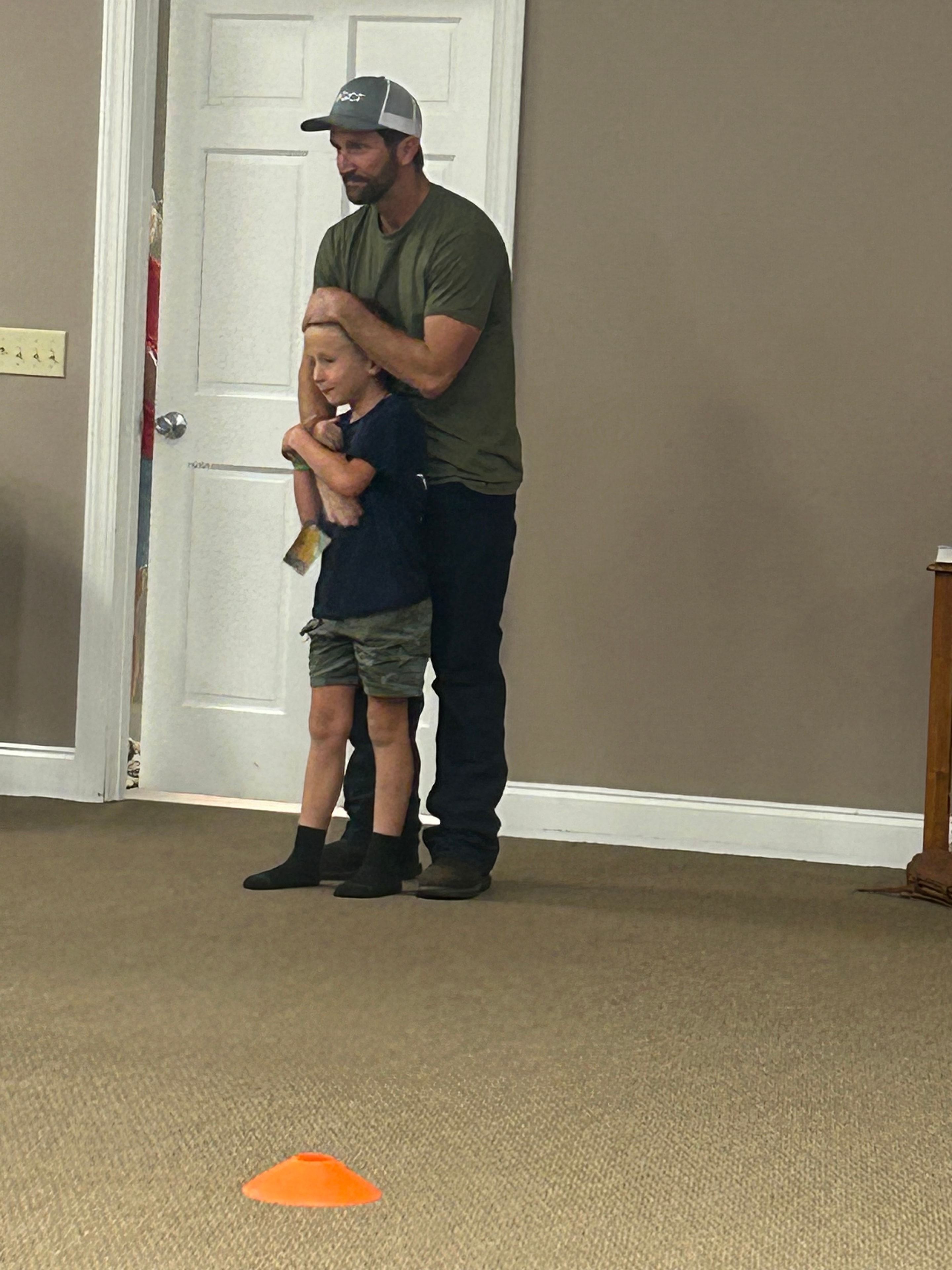 Man lifting a young boy near a doorway with orange cones at VBS 2026